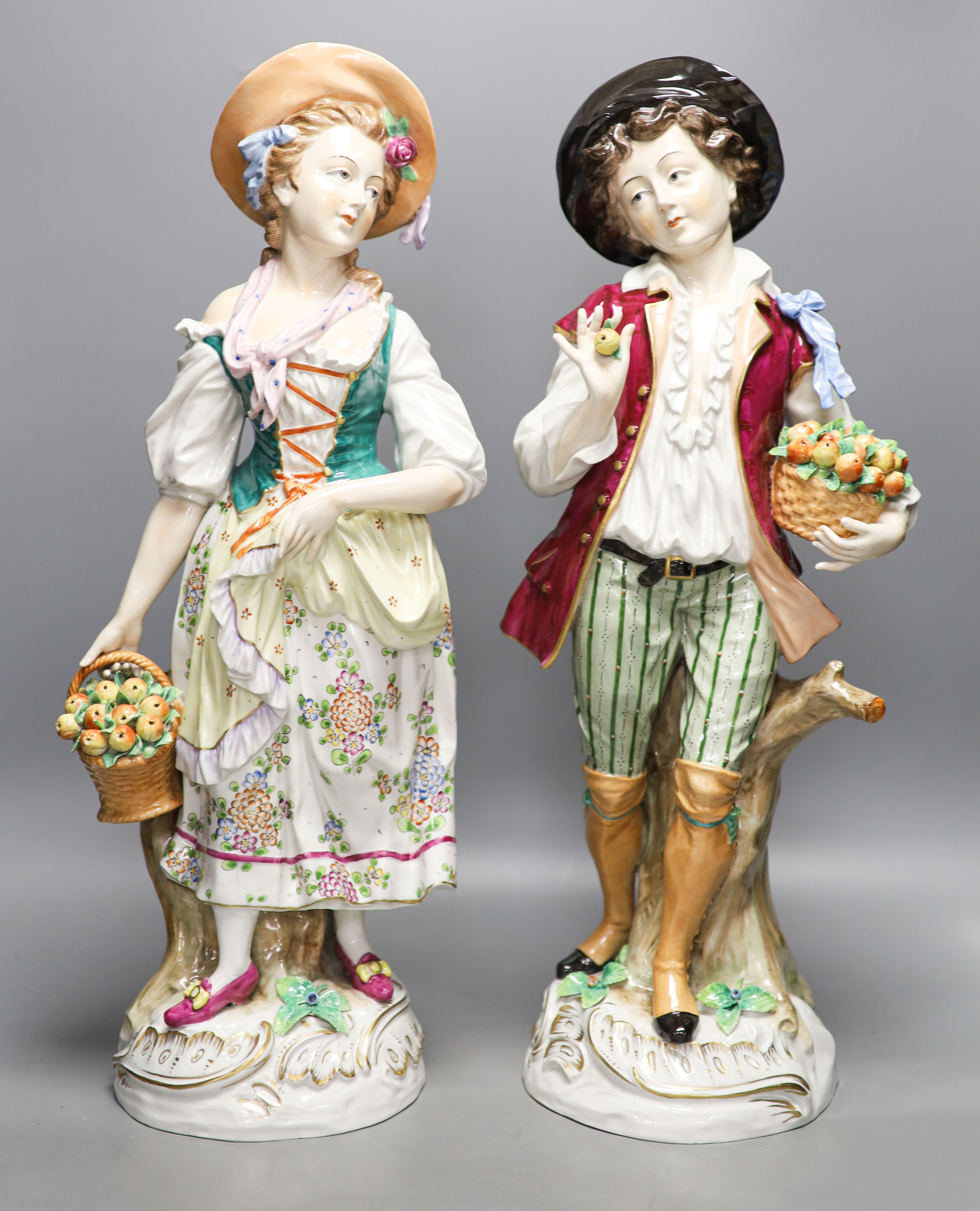 A pair of large Sitzendorf porcelain figures of a maid and a gallant, carrying baskets of fruit 52cm